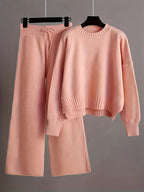 Pink knit sweater and pants set on hangers against a gray background