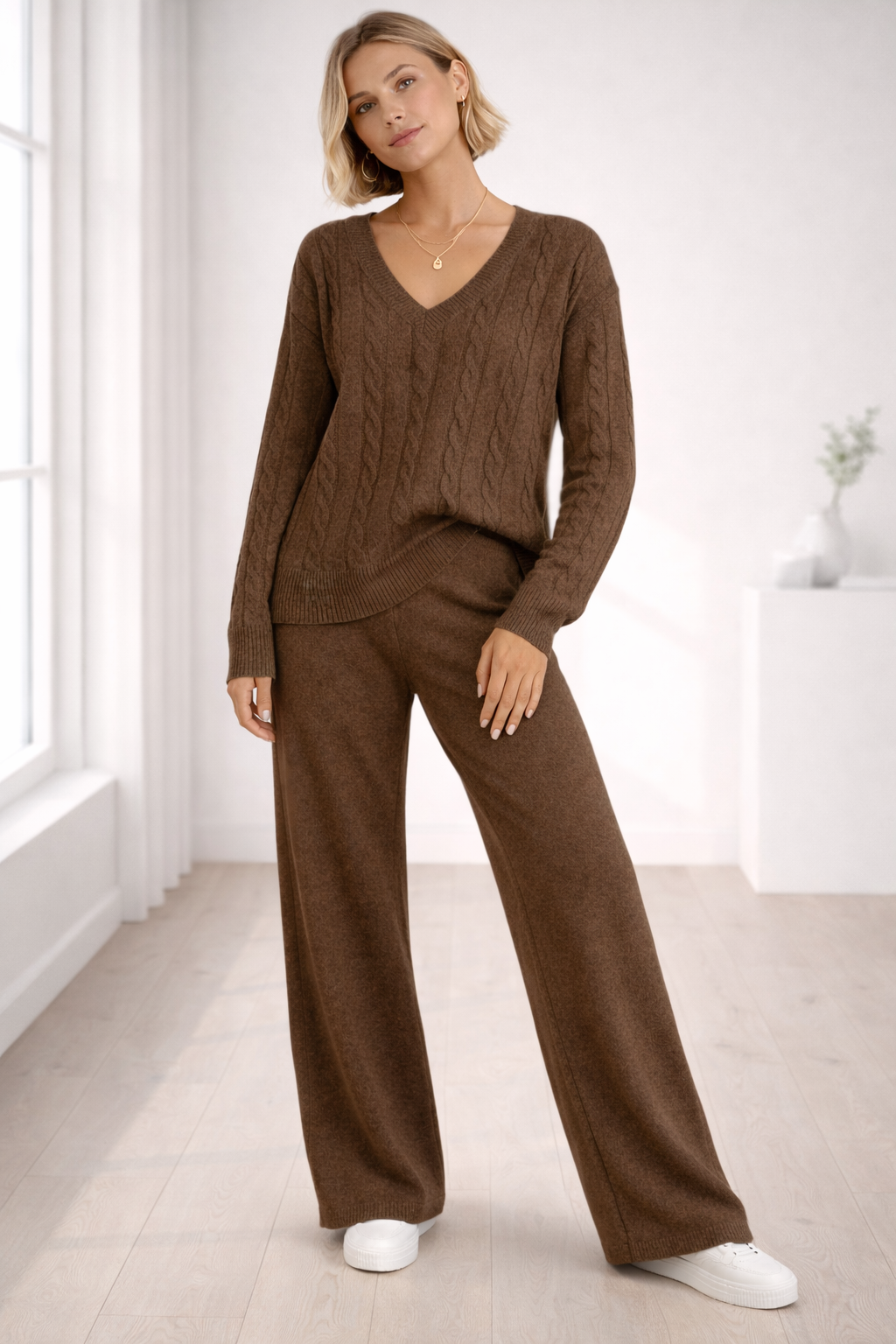 Woman wearing a brown cable knit sweater and pants in a bright room.