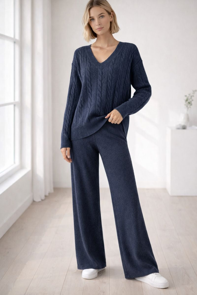 Woman wearing a navy blue cable knit sweater and pants in a bright room.