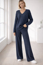 Woman wearing a navy blue cable knit sweater and pants in a bright room.