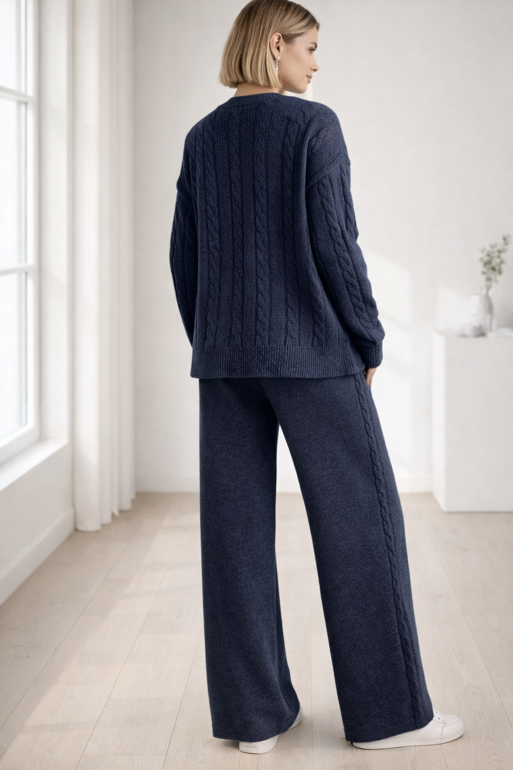 Woman wearing a navy cable knit sweater and pants in a minimalistic room.