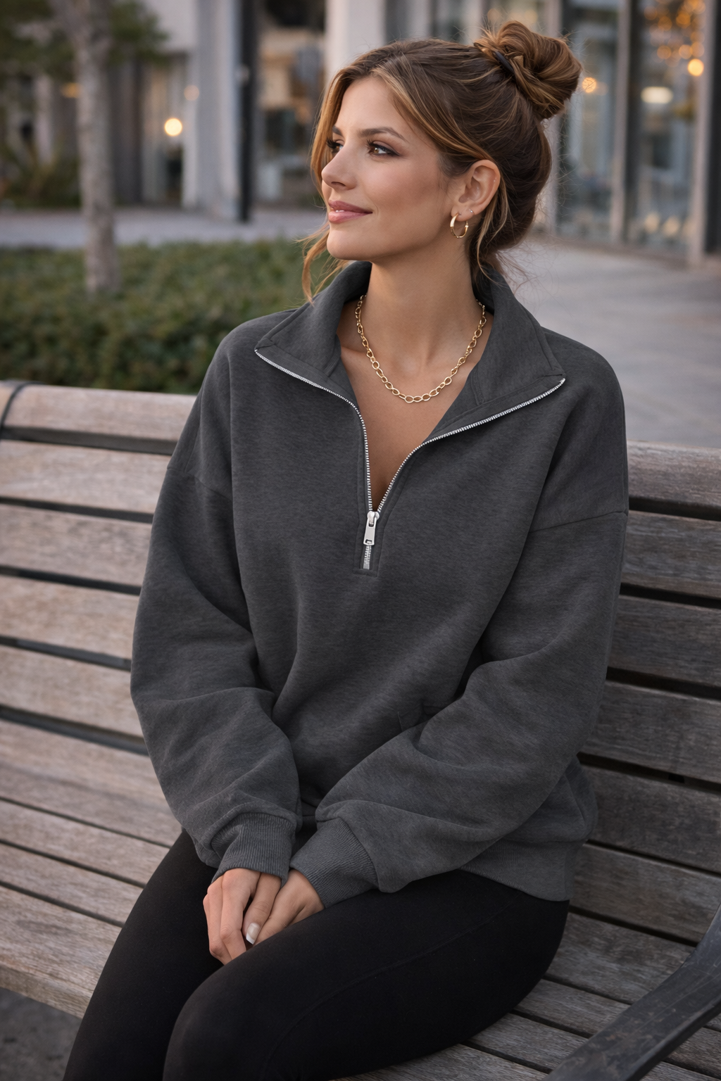 Woman sitting on a bench wearing a gray zip-up sweatshirt.
