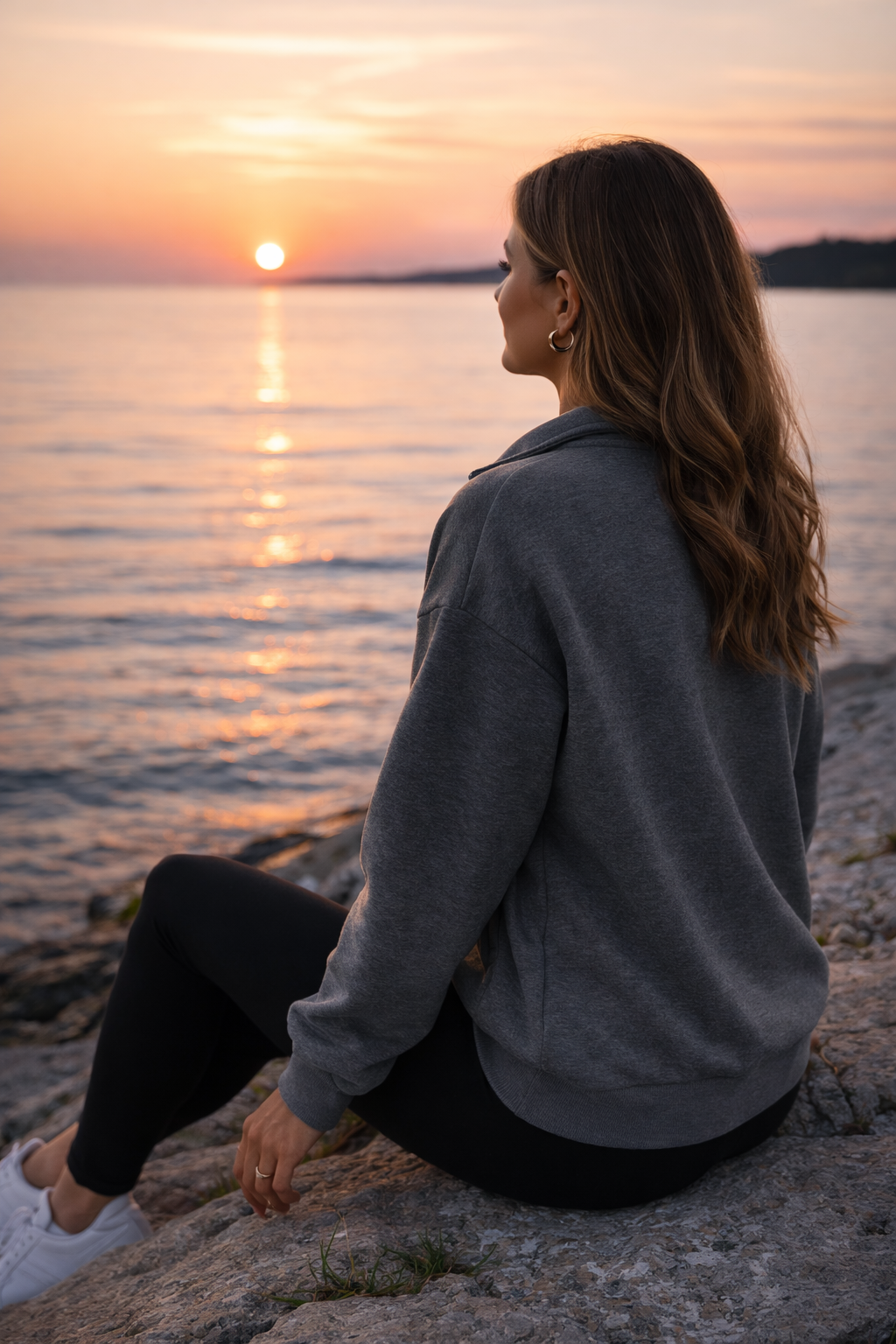 Woman sitting on a rock by the water at sunset