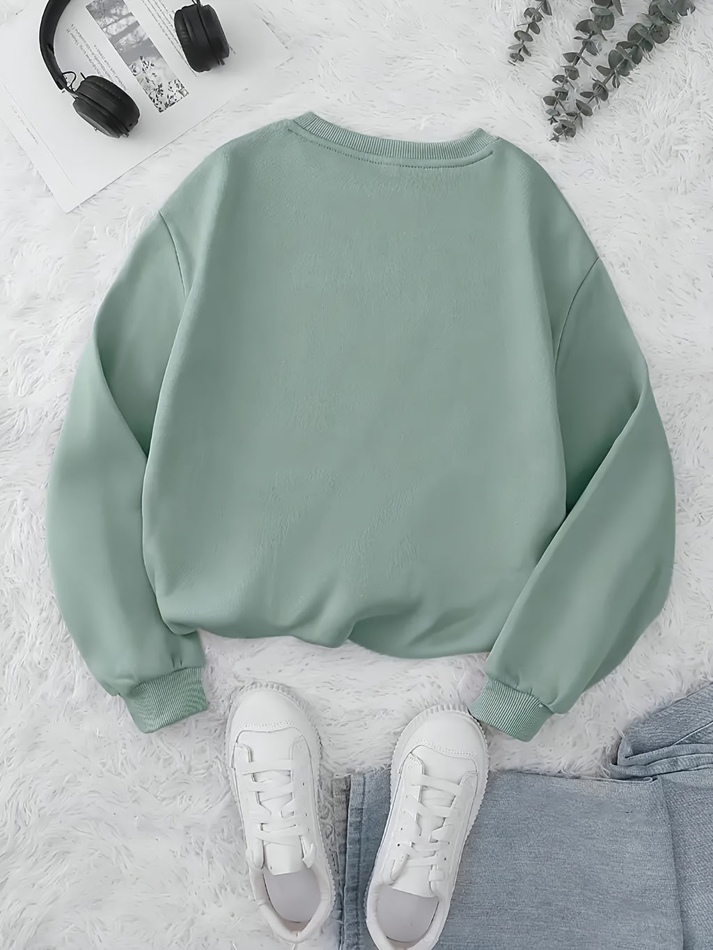 Green sweatshirt on a light gray surface with white sneakers and a pair of headphones.