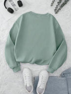 Green sweatshirt on a light gray surface with white sneakers and a pair of headphones.