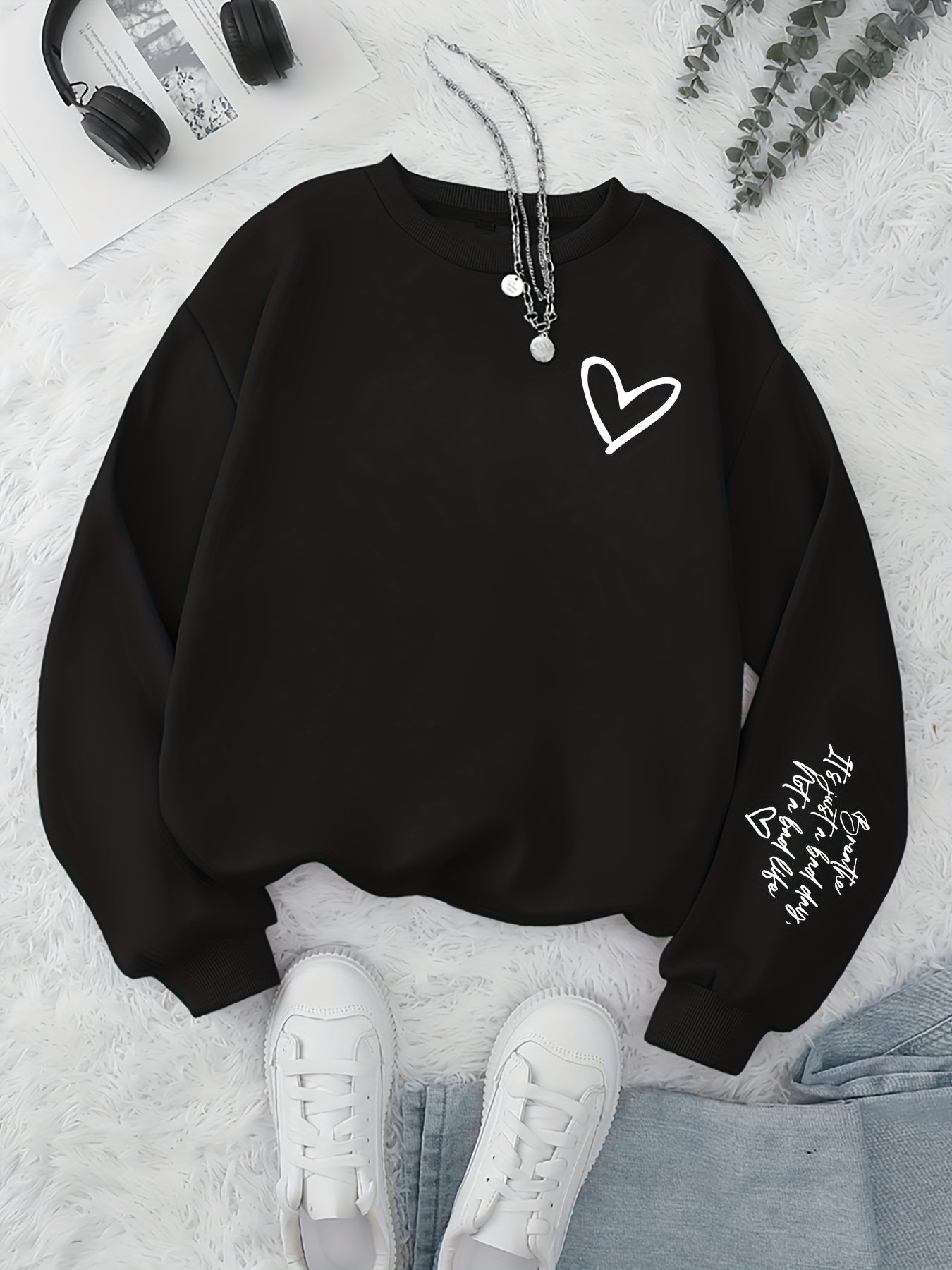 Black sweatshirt with a heart design on a light gray surface with sneakers and headphones.
