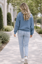 Woman walking on a path wearing a blue sweatshirt and light blue jeans.
