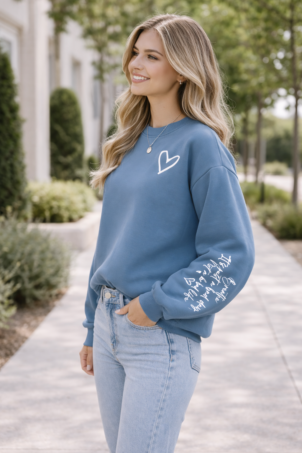 Woman wearing a blue sweatshirt with a heart design and text, standing outdoors.
