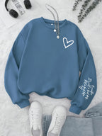 Blue sweatshirt with a heart design on a light gray surface with sneakers and headphones.