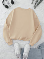 Beige sweatshirt on a white surface with white sneakers and gray pants.