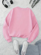 Pink sweatshirt on a textured surface with white sneakers and headphones.