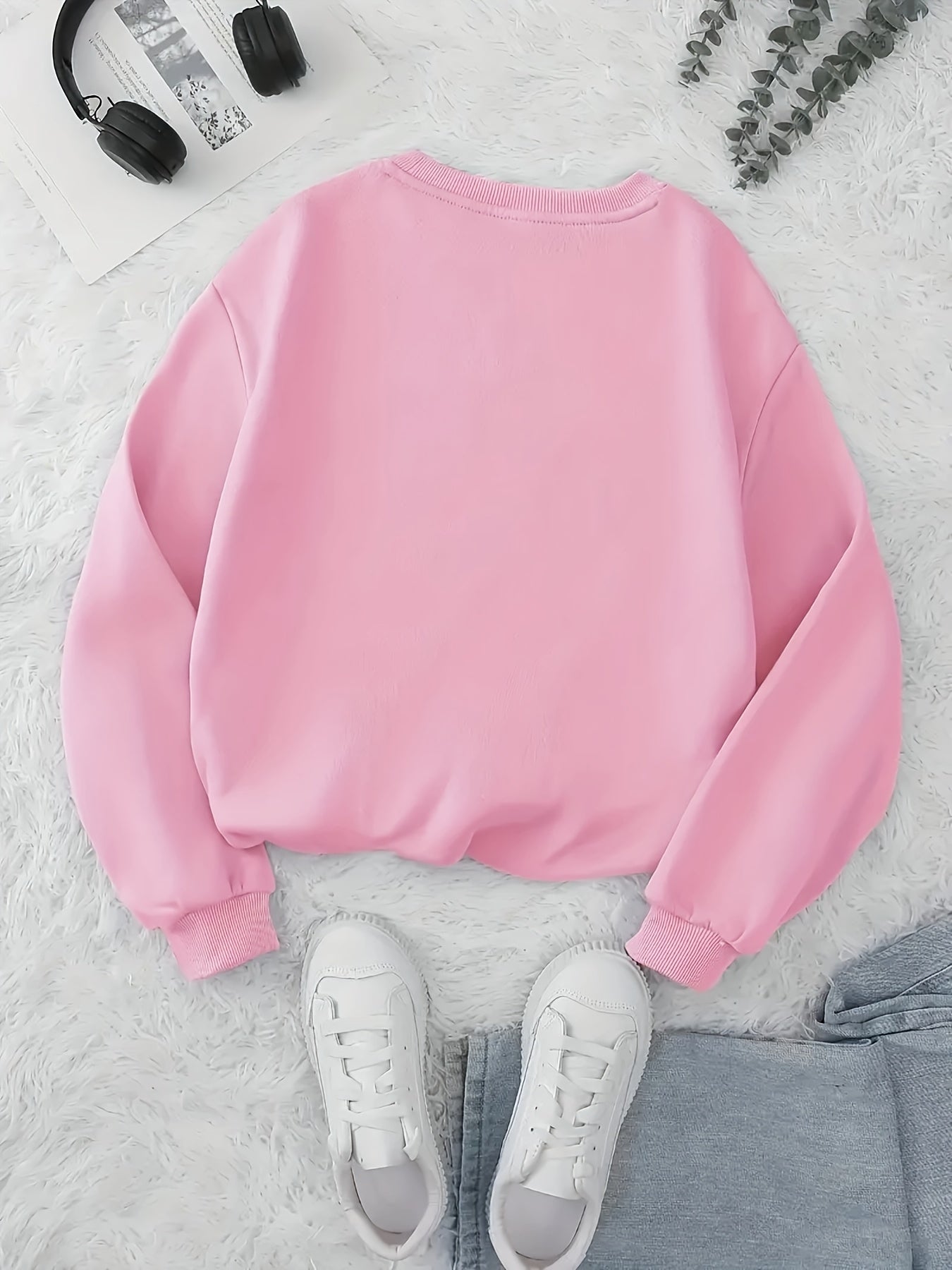 Pink sweatshirt on a textured surface with white sneakers and headphones.