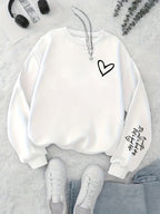 White sweatshirt with black heart design on a light gray surface with sneakers and headphones.