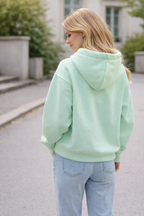 Person wearing a light green hoodie and light blue jeans walking outdoors.