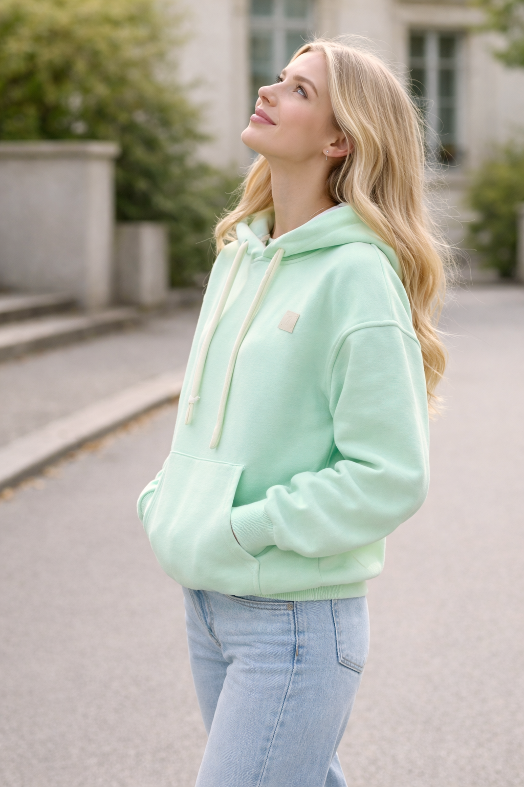 Woman wearing a light green hoodie and blue jeans standing outdoors.