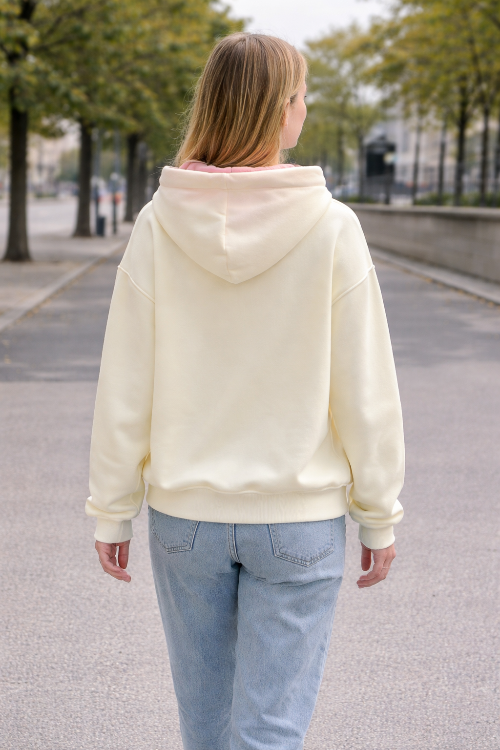 Person wearing a light-colored hoodie and blue jeans walking on a street.