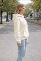 Woman wearing a light-colored hoodie and jeans walking on a street.