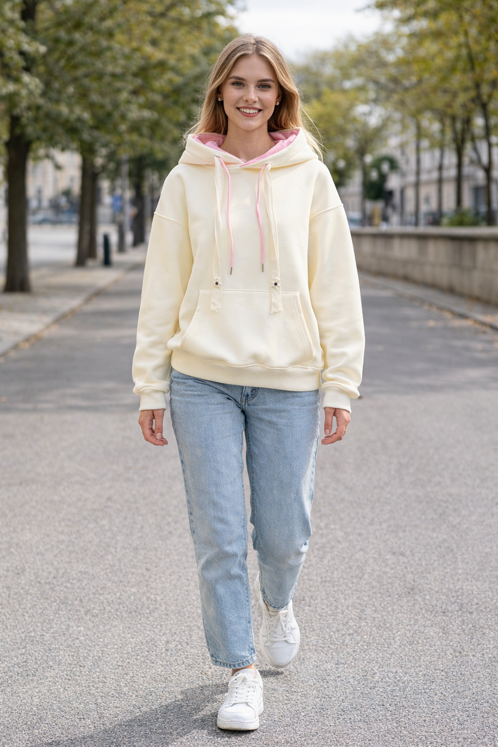 Woman wearing a light-colored hoodie and jeans walking on a street.