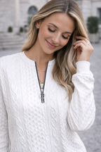 Woman wearing a white cable knit sweater with a zipper, standing outdoors.