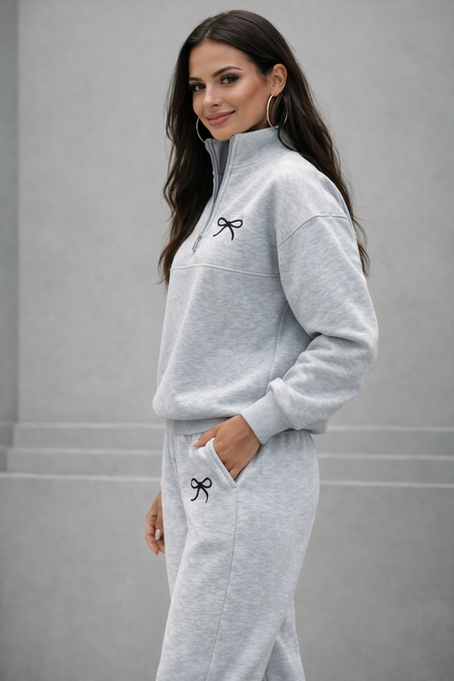 Woman wearing a gray tracksuit with a bow design on a plain background