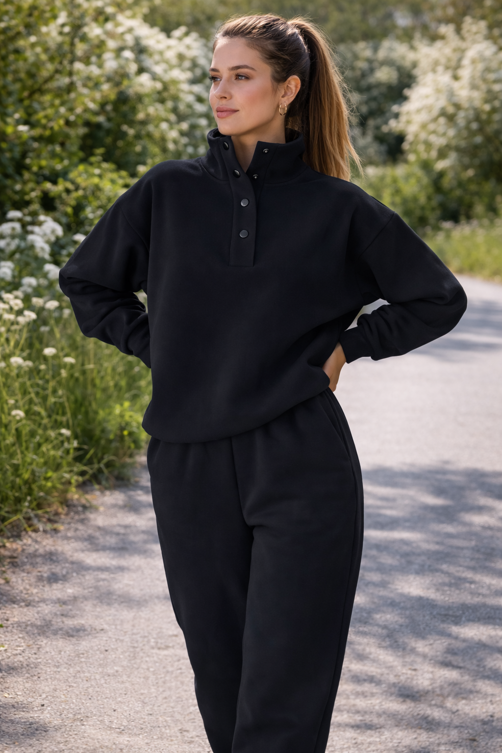 Woman in a black outfit standing on a path with greenery and flowers in the background