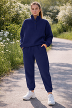 Woman wearing a navy blue tracksuit standing on a path with greenery around.