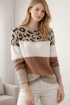 Woman wearing a leopard print and color-blocked sweater with white pants against a neutral background
