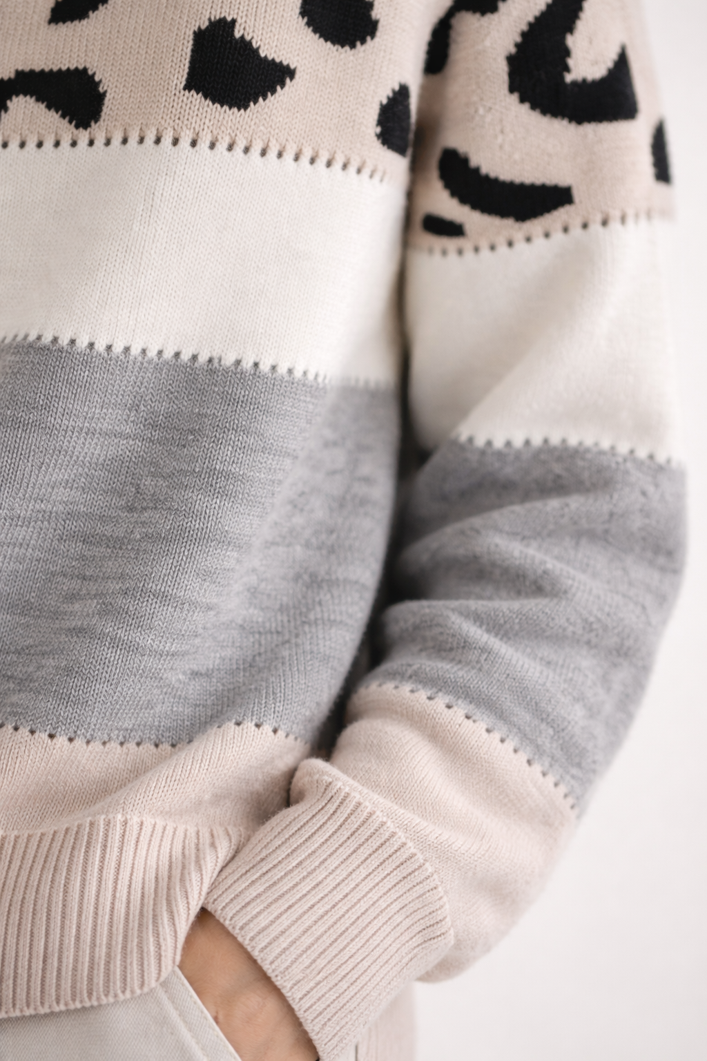 Close-up of a sweater with leopard print pattern, gray sleeves, and beige body.