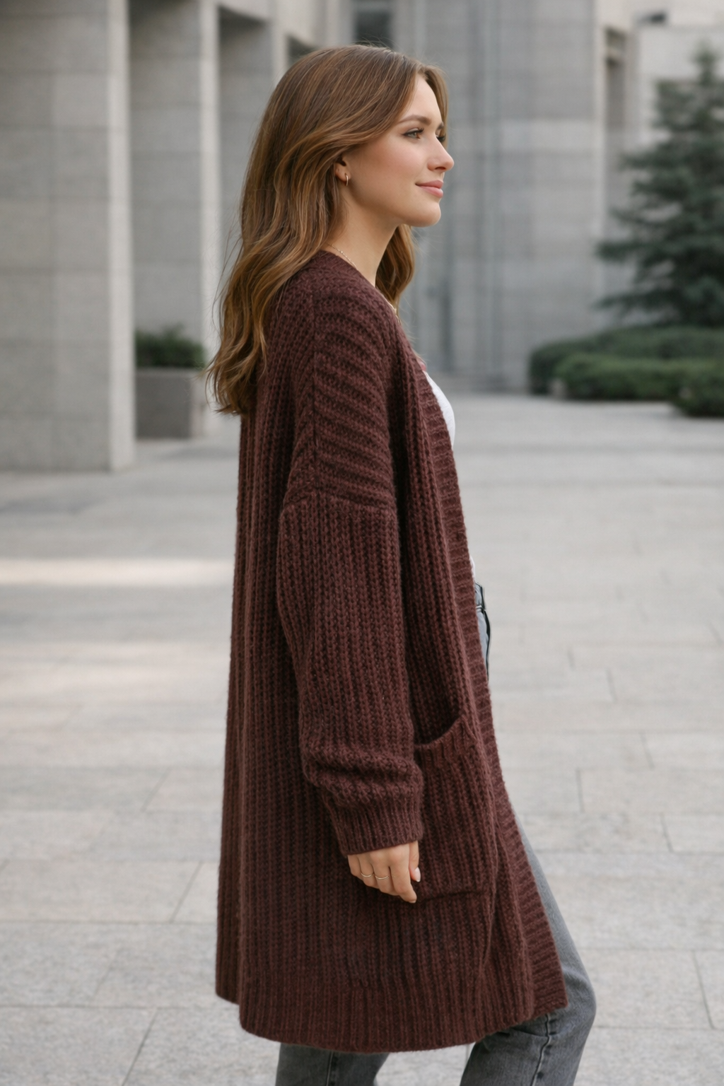 Woman wearing a brown cardigan standing outdoors on a city street.