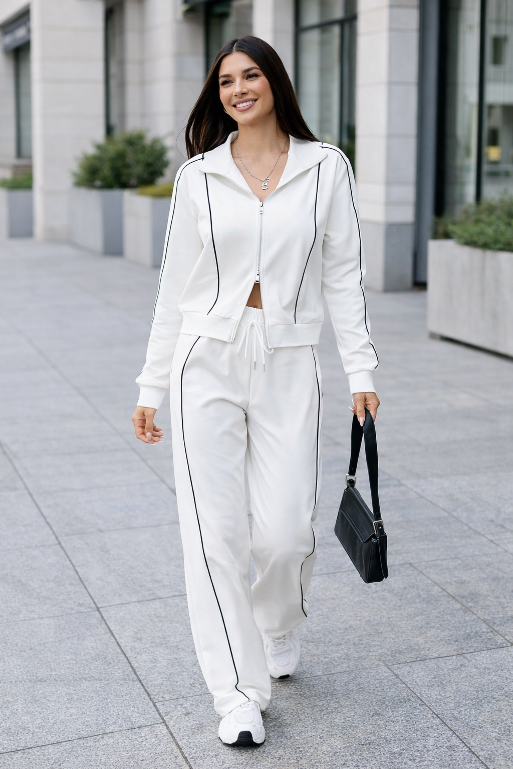 Woman in a white outfit with black accents walking outdoors.