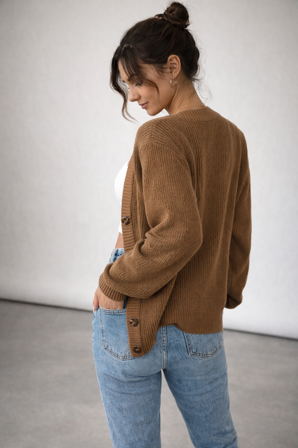 Woman wearing a brown cardigan and blue jeans against a plain background