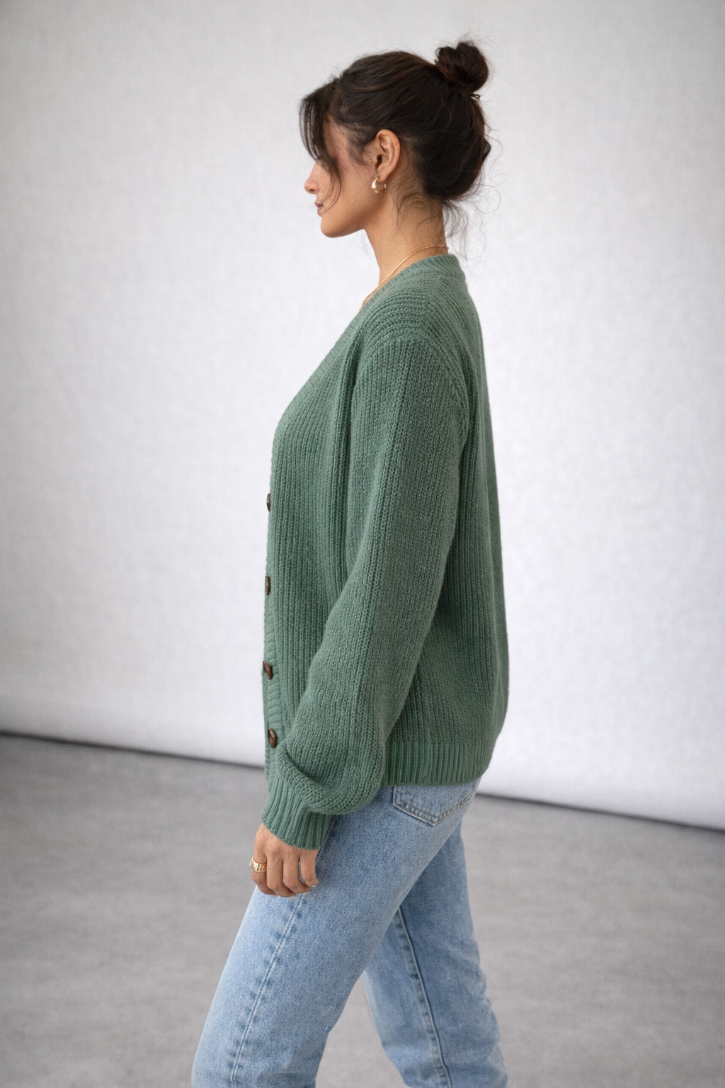 Woman wearing a green sweater and light blue jeans against a white background