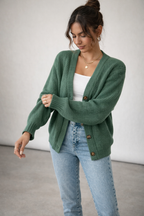 Woman wearing a green cardigan over a white top and blue jeans on a plain background