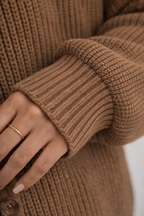 Close-up of a person wearing a brown knitted sweater with a white background