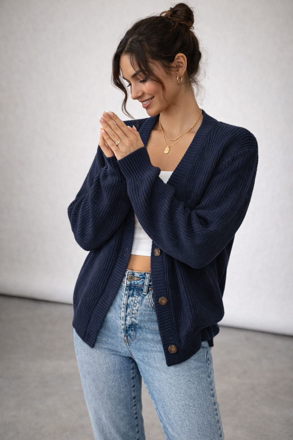 Woman wearing a navy blue cardigan over a white top and blue jeans, standing against a plain background.