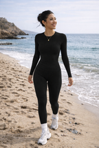 Woman in black long-sleeve top and leggings standing on a beach with ocean in the background