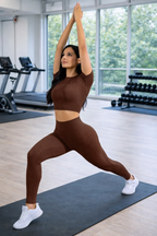 Woman in brown athletic wear performing a yoga pose in a gym.